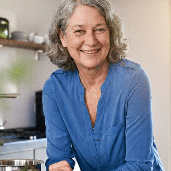 About us 2 Me smiling in my home kitchen, standing behind a pot and fresh vegetables on the counter